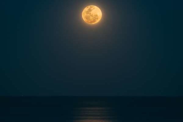 A yellowish moon hangs over a dark ocean