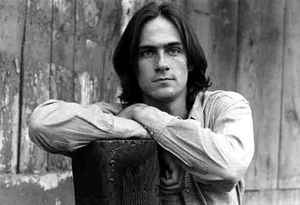 James Taylor, with his arms resting on a tree stump.