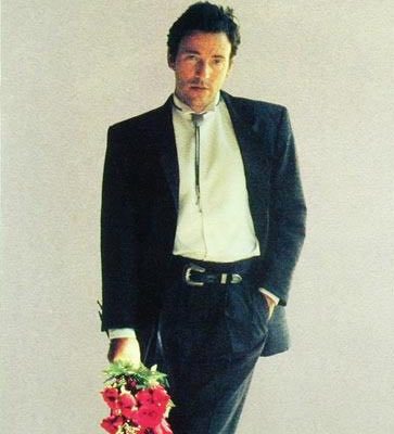Bruce Springsteen, in a black suit holding a bouquet of red flowers.